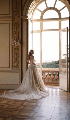 a woman in a wedding dress looking out an open door at the view from her balcony