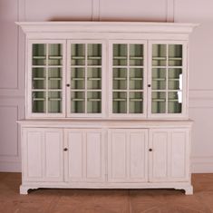 a white china cabinet with glass doors on the top and bottom, against a pink wall