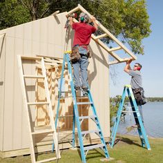 two men are working on the roof of a house that's being built next to water