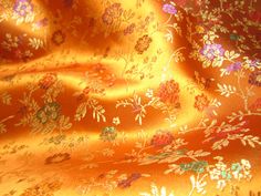 an orange fabric with flowers and leaves is shown in close up view on the surface