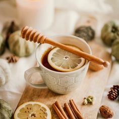 a cup of tea with cinnamon, lemon and honey on a wooden cutting board next to pumpkins