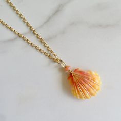 an orange shell is hanging from a gold chain on a white marble counter top,