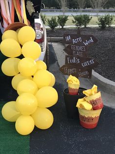 yellow balloons are on the ground next to some signs and buckets with food in them