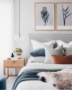 a bed with pillows and blankets on top of it, next to two framed pictures