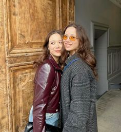 two women standing next to each other in front of a wooden door with sunglasses on