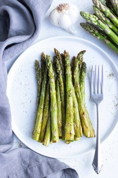 asparagus on a white plate with garlic and seasoning next to it, ready to be eaten