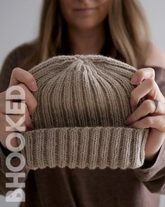 a woman holding up a knitted hat with the word shocked on it in front of her face