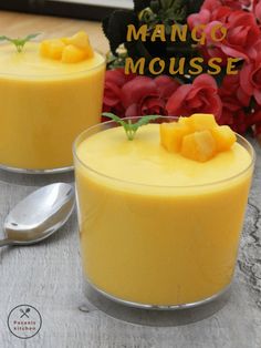 two glasses filled with mango mousse sitting on top of a table next to flowers