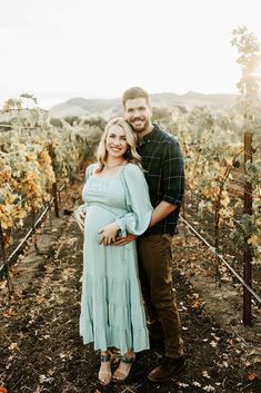 a pregnant couple standing in the middle of a vineyard