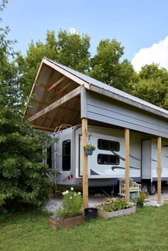 an rv is parked under a wooden structure in the grass near some trees and bushes