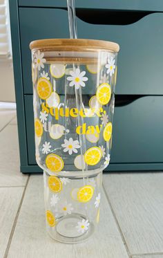 a glass cup with lemons and daisies painted on it is sitting on the floor