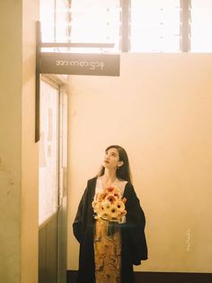 a woman standing in front of a doorway with flowers on her lap and looking up at the sky