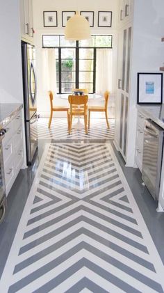 a kitchen with white cabinets and gray and white chevron tile flooring that has a dining room table in the center