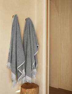 two towels hanging on the wall next to a wooden table with a stool underneath it