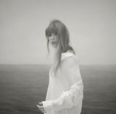 a woman with long hair standing in front of the ocean