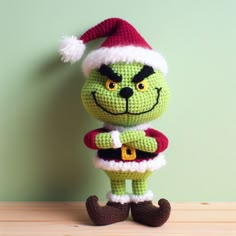 a crocheted grin face doll is posed on a wooden table with a green wall in the background