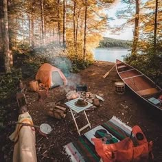 there is a tent and campfire in the woods next to some canoes on the ground