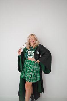 a woman in a green and black outfit is holding an umbrella while standing against a white wall