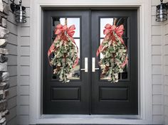 two christmas wreaths on the front door of a gray house with black double doors