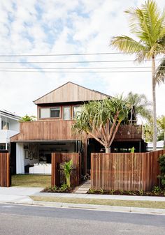 a house with wooden fence and palm trees in front of it on the side of the road