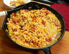 a skillet filled with corn on top of a wooden table