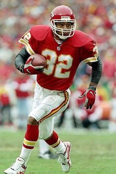 a football player is running with the ball in his hand and wearing red, white and yellow