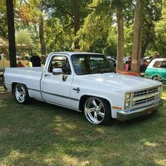 a white pickup truck parked on top of a grass covered field next to trees and other vehicles