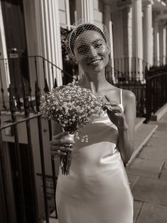 a woman in a white dress holding a bouquet of flowers on the side of a street