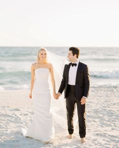 a bride and groom holding hands on the beach