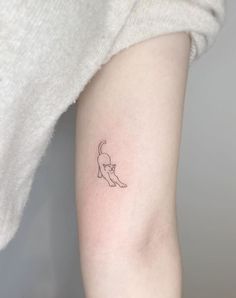 a small cat tattoo on the left inner arm and shoulder, with an outline of a cat