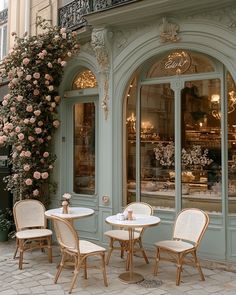 three chairs and two tables in front of a building with flowers on the outside wall