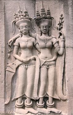 two women are standing next to each other in front of a stone wall with carvings on it