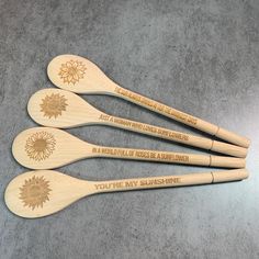 four wooden spoons with engraved words on them sitting next to each other in front of a gray background