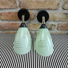 two green lamps sitting on top of a black and white striped table cloth next to a brick wall