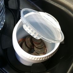 a plastic container filled with coins sitting on top of a black car dash board next to a water bottle