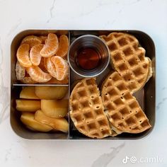 a metal container filled with waffles, orange slices and syrup next to sliced fruit