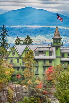 a green building with a flag on top and mountains in the backgroung