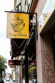 a yellow sign hanging from the side of a building next to a sidewalk with people walking on it