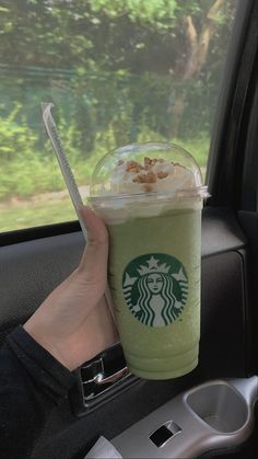 a starbucks drink is being held up in the back seat of a car by someone's hand