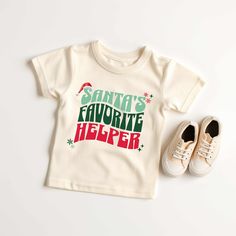 "Kids will look adorable in this \"SANTA'S FAVORITE HELPER\" youth short sleeve tee. This lightweight side-seamed shirt maximizes comfort all day long.  Santa's Favorite Helper Kids Toddler Youth, Christmas T Shirt, Santa Shirts for Kids, Boy Kids Holiday Outfit Holiday Shirts 🌟100% Airlume combed and ringspun cotton (fiber content may vary for different colors) 🌟Light fabric (3.9 oz/yd² (132 g/m 🌟Retail fit RETURNS: All products are made-to-order and because of the nature of these items, all Cute Short Sleeve T-shirt For Winter, Christmas Cotton Short Sleeve Shirt, Cute Holiday Tops With Short Sleeves, Cute Short Sleeve Holiday Tops, Pre-shrunk Short Sleeve Christmas Tops, Cute Christmas T-shirt With Letter Print, Festive Holiday Short Sleeve T-shirt, Festive Short Sleeve Cotton Tops, Holiday Cotton Short Sleeve Shirt