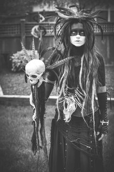 a woman with long hair and makeup holding a skull in front of her face,