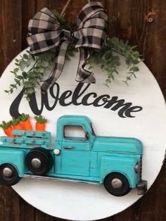 a welcome sign with an old blue pickup truck and carrots on it, hanging on a wooden fence