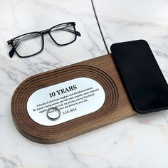 a wooden plaque with a ring and glasses on it next to a cell phone that reads 10 years