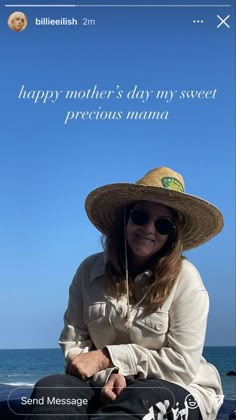 a woman sitting on the beach wearing a hat and sunglasses