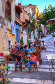 several people sitting at tables in the middle of an alleyway with umbrellas over them