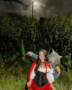 a woman in a red dress holding a stuffed animal on her back while sitting next to a hedge