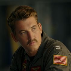 a man with a mustache and an american flag patch on his shirt is looking at the camera