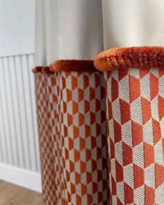 two orange and white vases sitting next to each other on a wooden floor in front of a wall