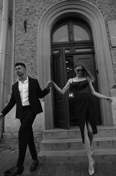 a man and woman are holding hands while walking down the street in front of a building