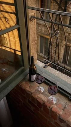 two wine glasses and a bottle sitting on a window sill in front of a building